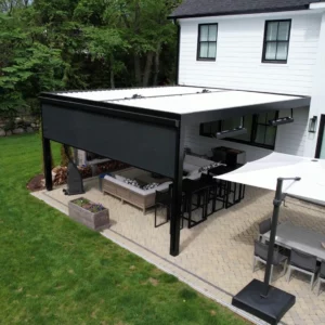 Elevated view of a modern outdoor living space with black pergola, retractable shades, and stylish patio furnishings adjacent to a white contemporary home.