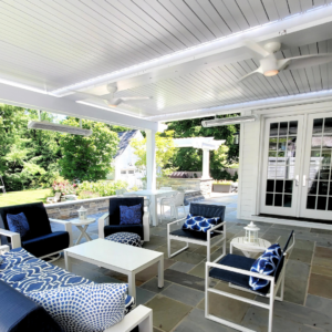 Outdoor lounging area with blue and white furniture under a motorized louvered pergola, surrounded by a lush garden.