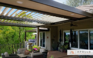 Elegant outdoor patio with a motorized louvered pergola providing adjustable shade, featuring comfortable seating, potted plants, and a view of lush greenery.