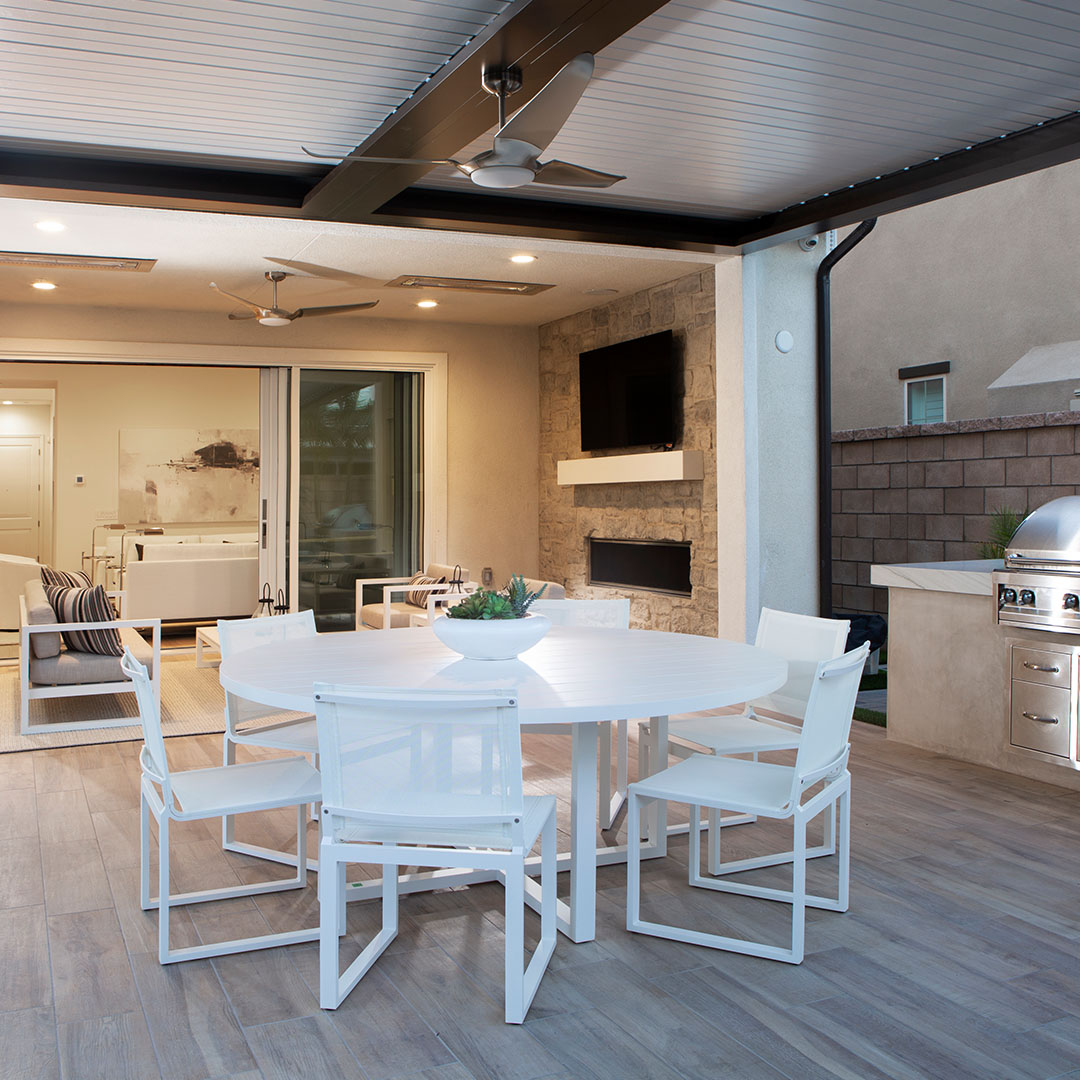 Seamlessly blended indoor-outdoor living space under a motorized louvered pergola, featuring a dining table and ceiling fans.