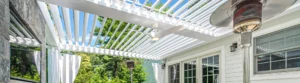 White louvered pergola on a patio with outdoor heaters and greenery in the background